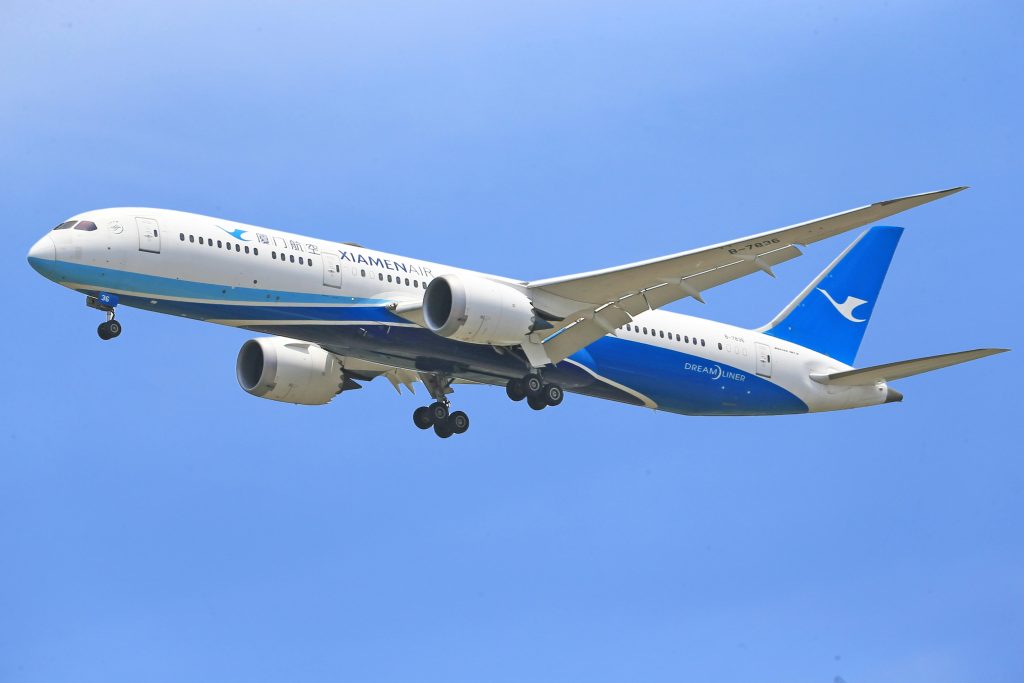 A Xiamen Air Boeing 787 Dreamliner flying in a clear blue sky, displaying aviation excellence.