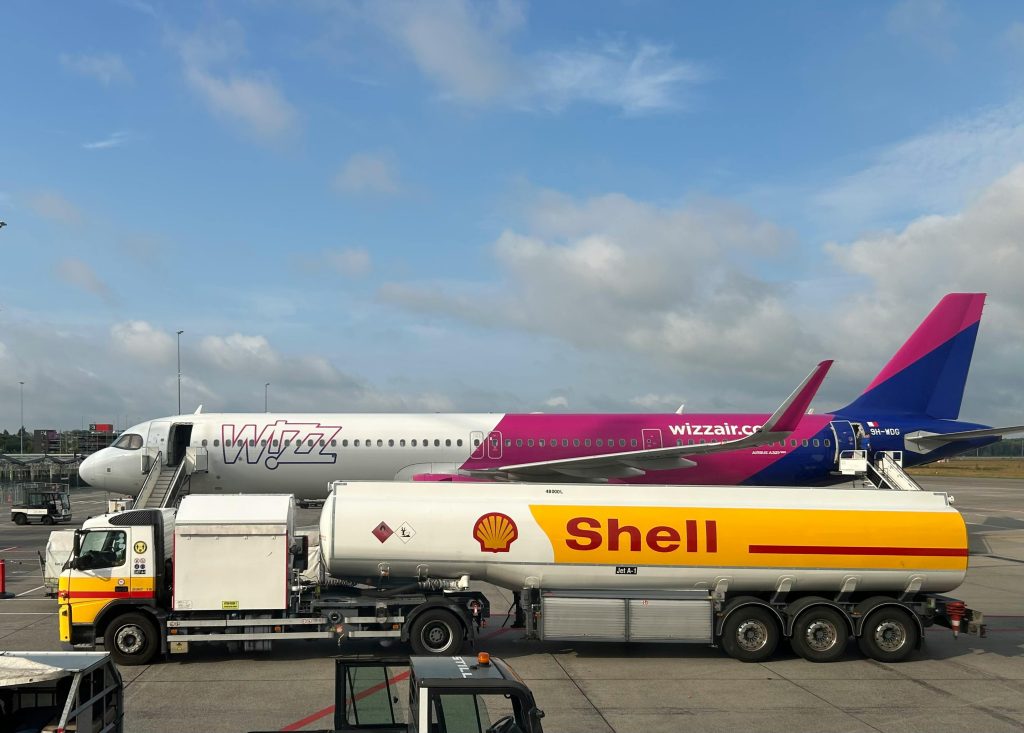 A plane being refueled by a Shell fuel truck on a sunny day at the airport.